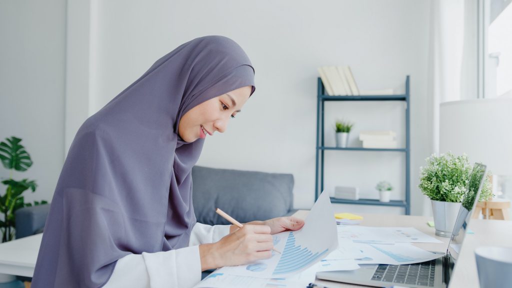 Beautiful Asia muslim lady in headscarf using laptop in living room at house.
